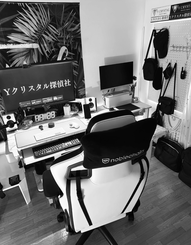 Yクリスタル探偵社の調査司令塔デスク。複数のモニターと壁には調査用バッグや機材が吊るされている。