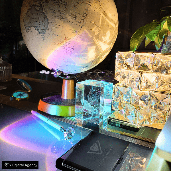 調査道具が置かれた机。羅針盤や地球儀、Yクリスタル探偵社のロゴが入った電卓、クリスタルペガサスのオブジェが配置され、虹色の光が反射している。