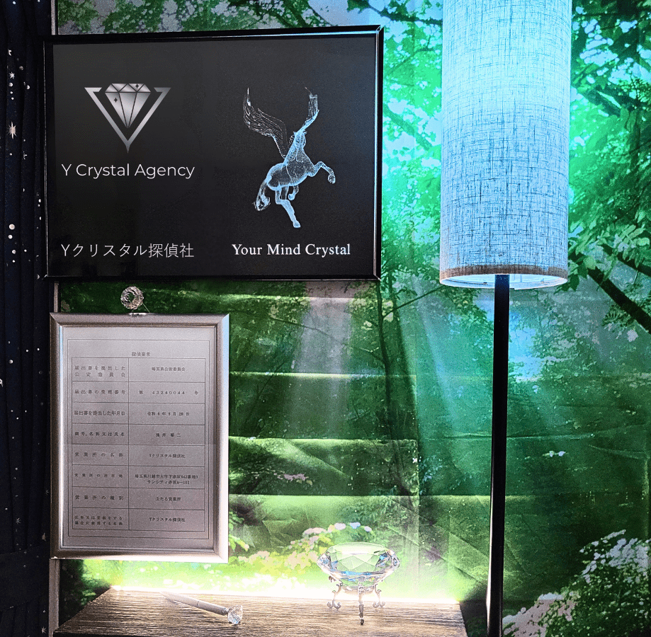 Yクリスタル探偵社のオフィス内観。白銀の額に入った探偵の標識、社名と「Your Mind Crystal」が記された浮き出し式内看板、そしてダイヤモンドのオブジェが間接照明に照らされ、幻想的な雰囲気を醸し出している。