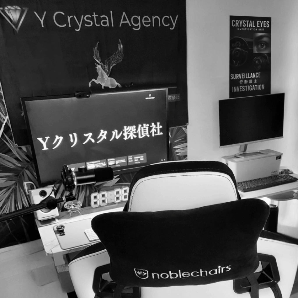 Yクリスタル探偵社のオフィス内部。デスクには複数のモニター、高機能なゲーミングチェア、そして探偵業務に必要な機材が並び、プロフェッショナルな調査環境を示している。